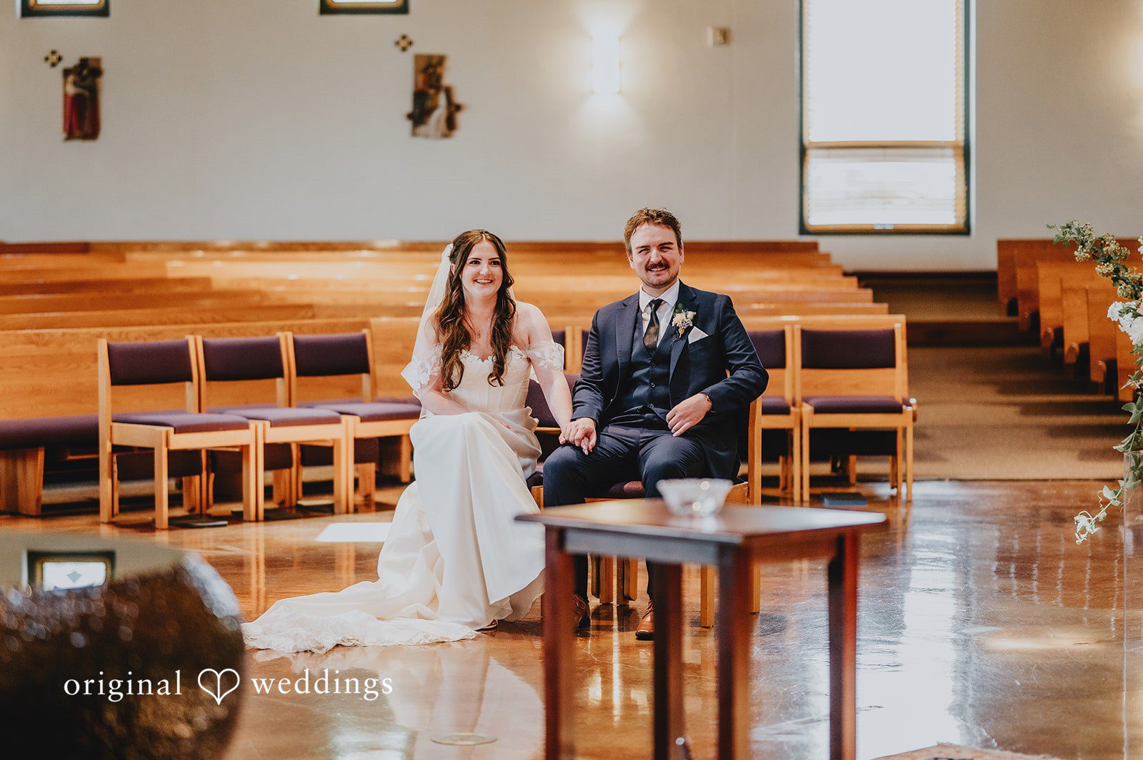 Bride and groom seated at a small table during the chapel ceremony.