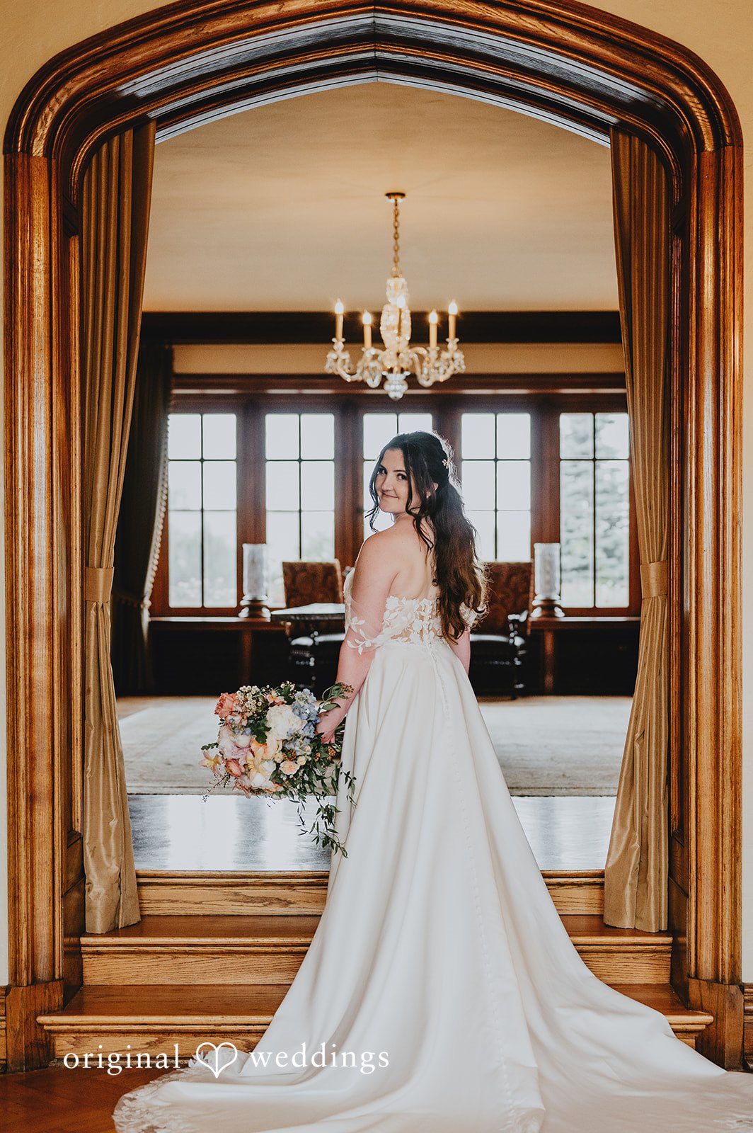 Bride from behind showing the full train of her wedding gown in a large arched doorway.