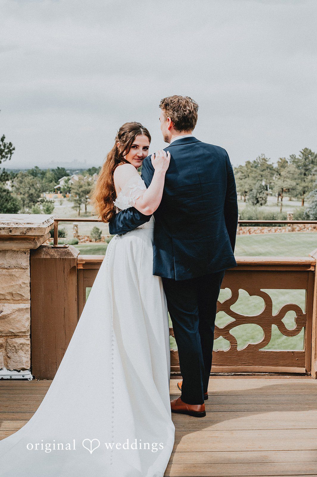 Bride and groom sharing an embrace on an elevated stone balcony.