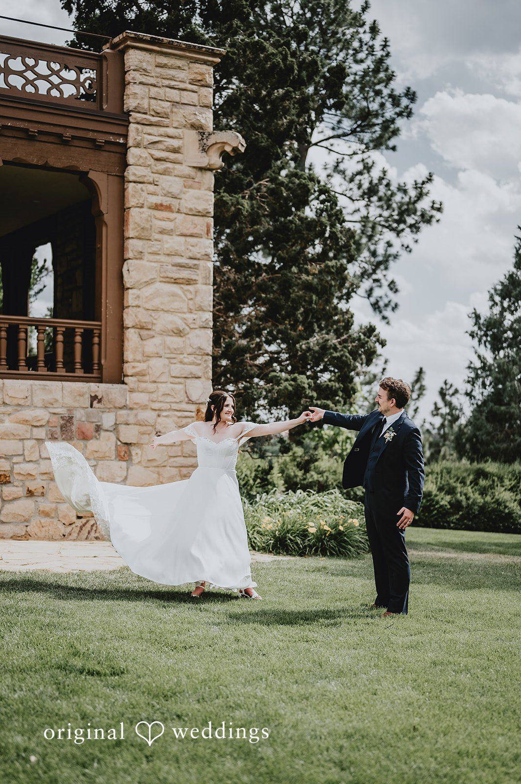 Groom watching the bride's long dress train flow on a green lawn.