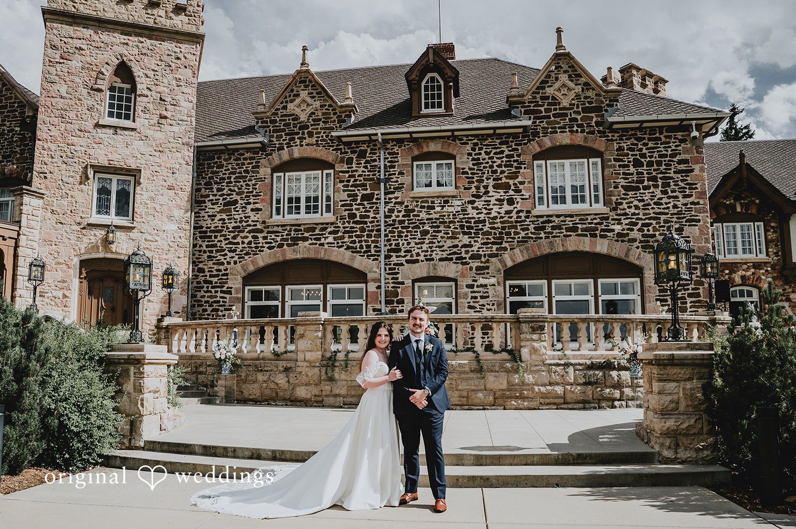 Bride and groom posing together closely in front of a grand stone mansion.