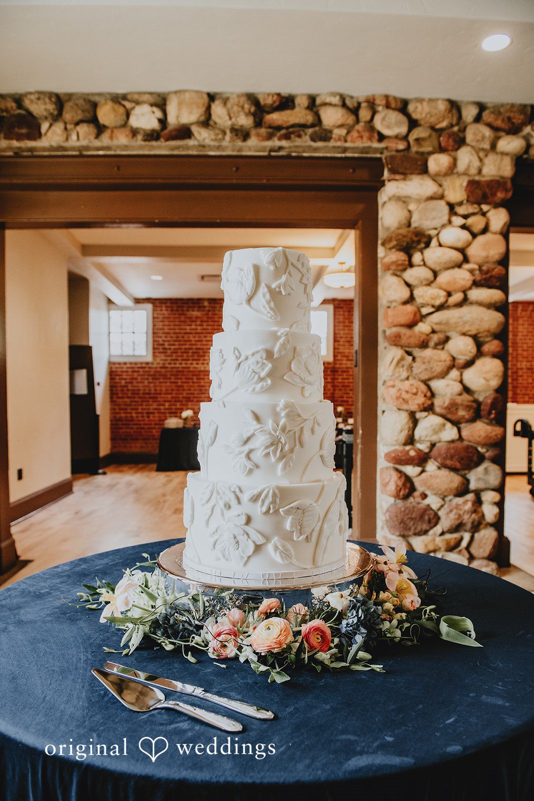 Multi-tiered white wedding cake decorated with flowers, displayed on a round table.