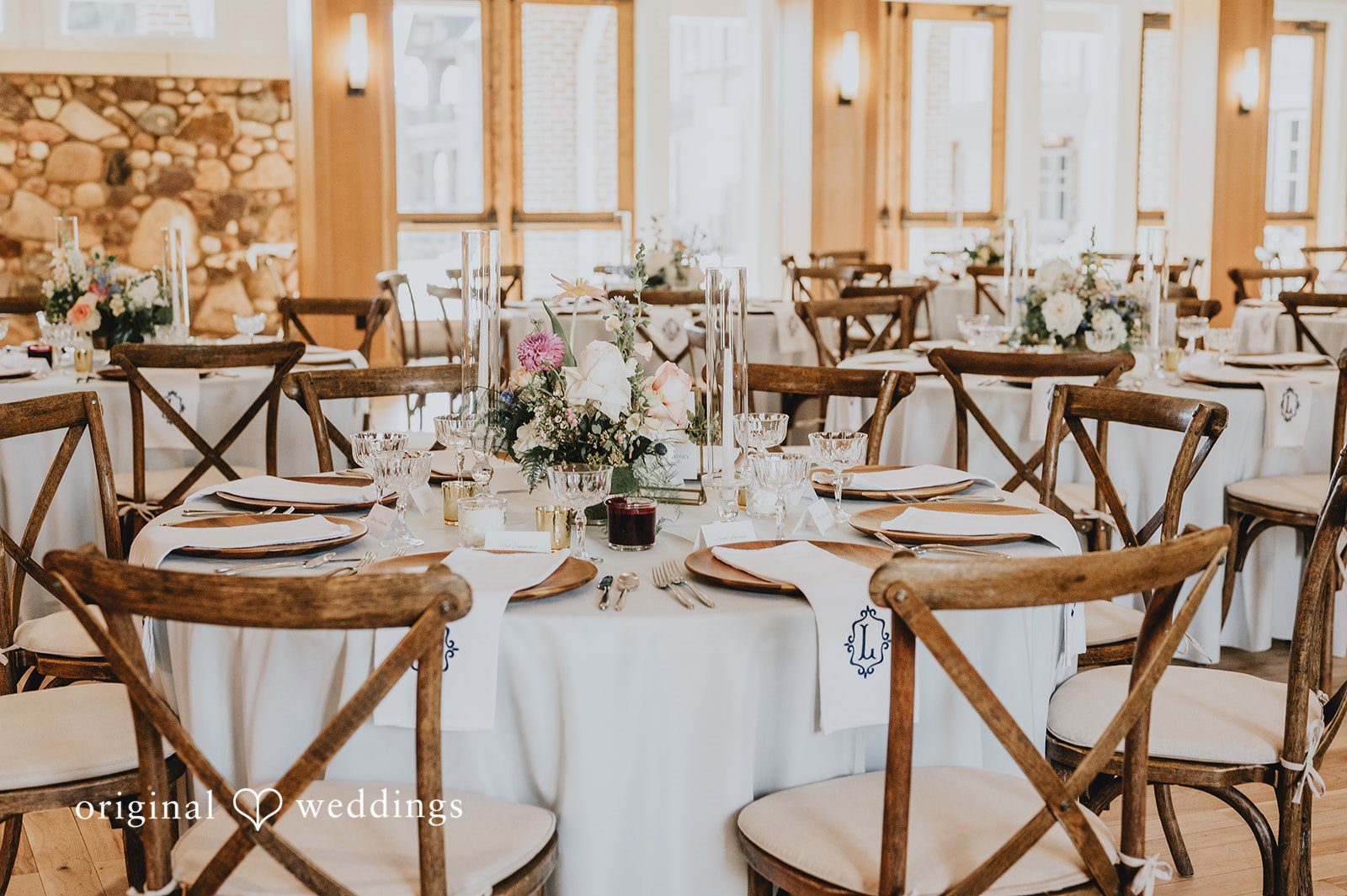 Circular wedding reception tables with wooden cross-back chairs and elegant table settings.