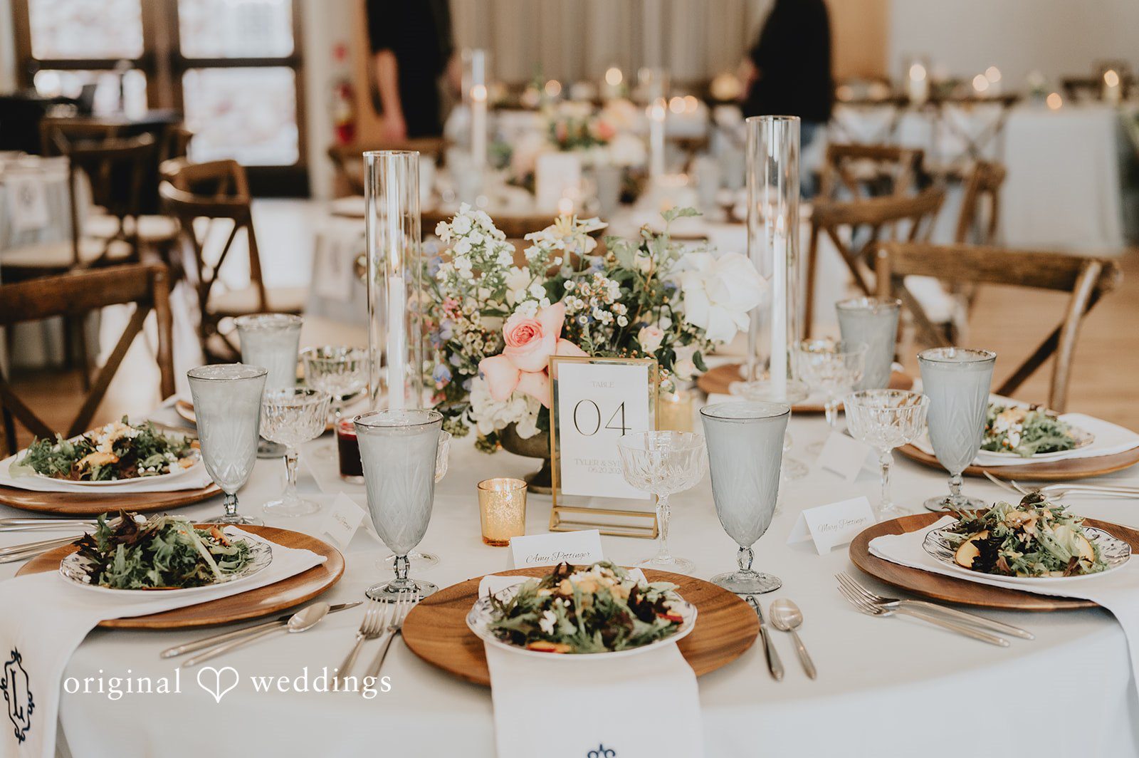 Long reception table set with white linens, crystal glassware, candles, and greenery garlands.
