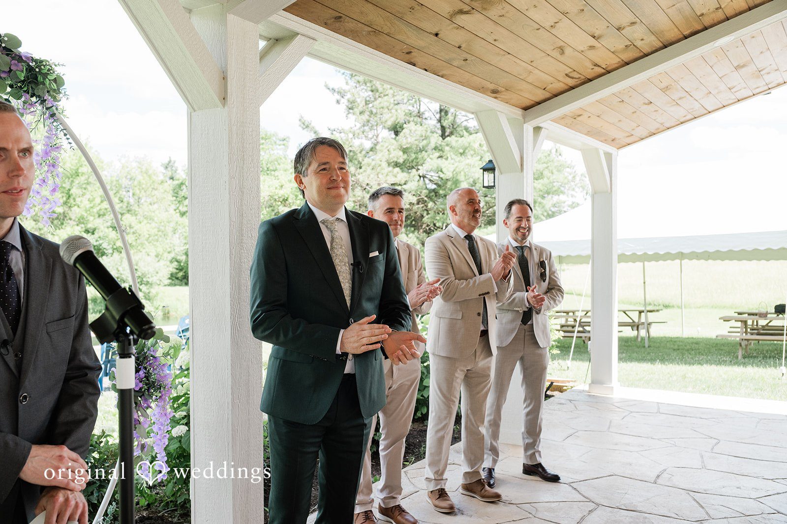 Carly + Seamus Groom and groomsmen standing together waiting under a wooden pavilion.