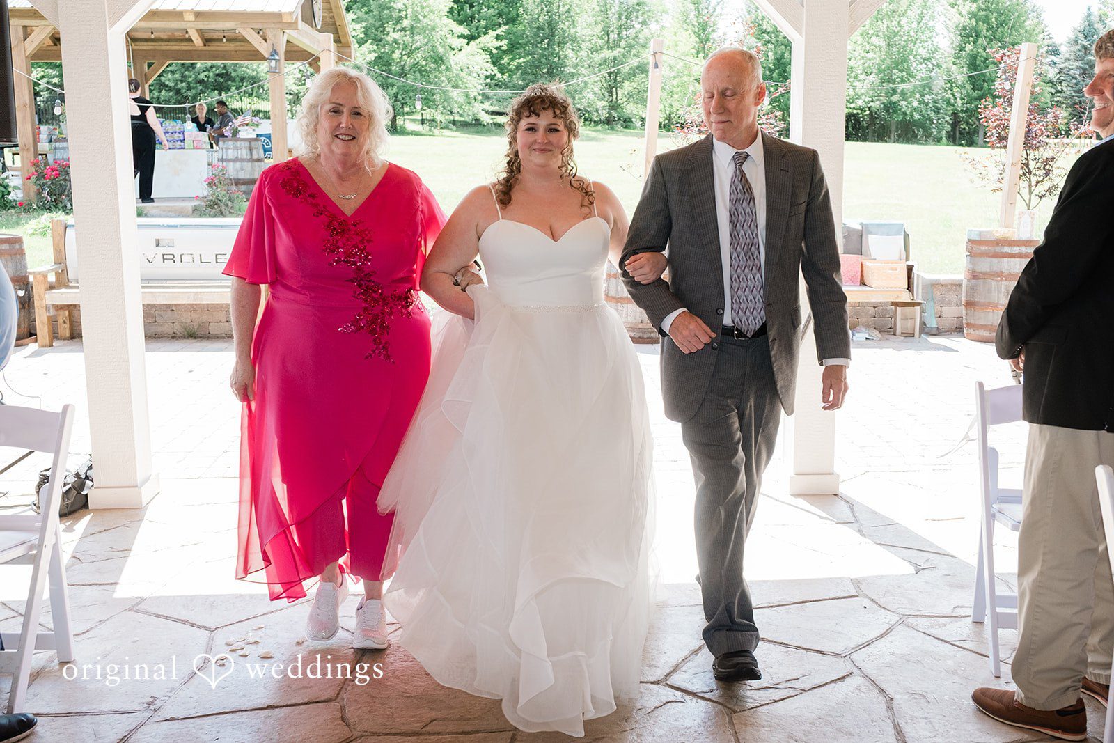 Carly + Seamus Bride walking down the aisle accompanied by two people.