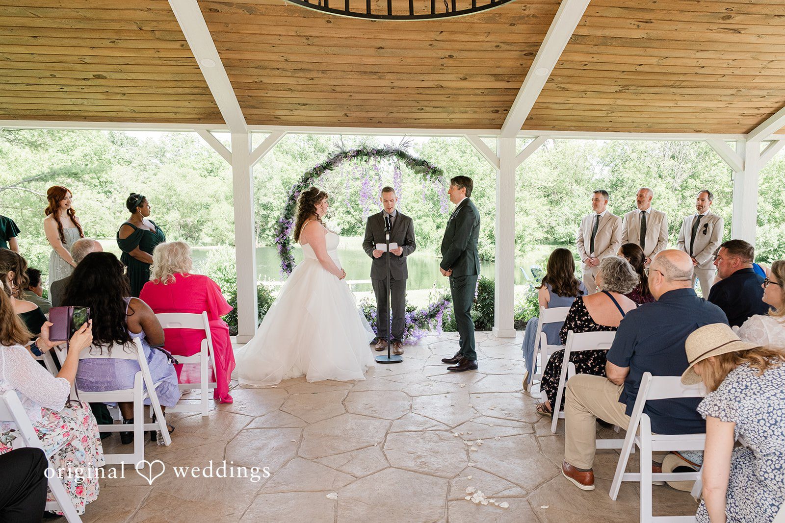 Carly + Seamus Wide view of guests seated for a wedding ceremony under a pavilion.