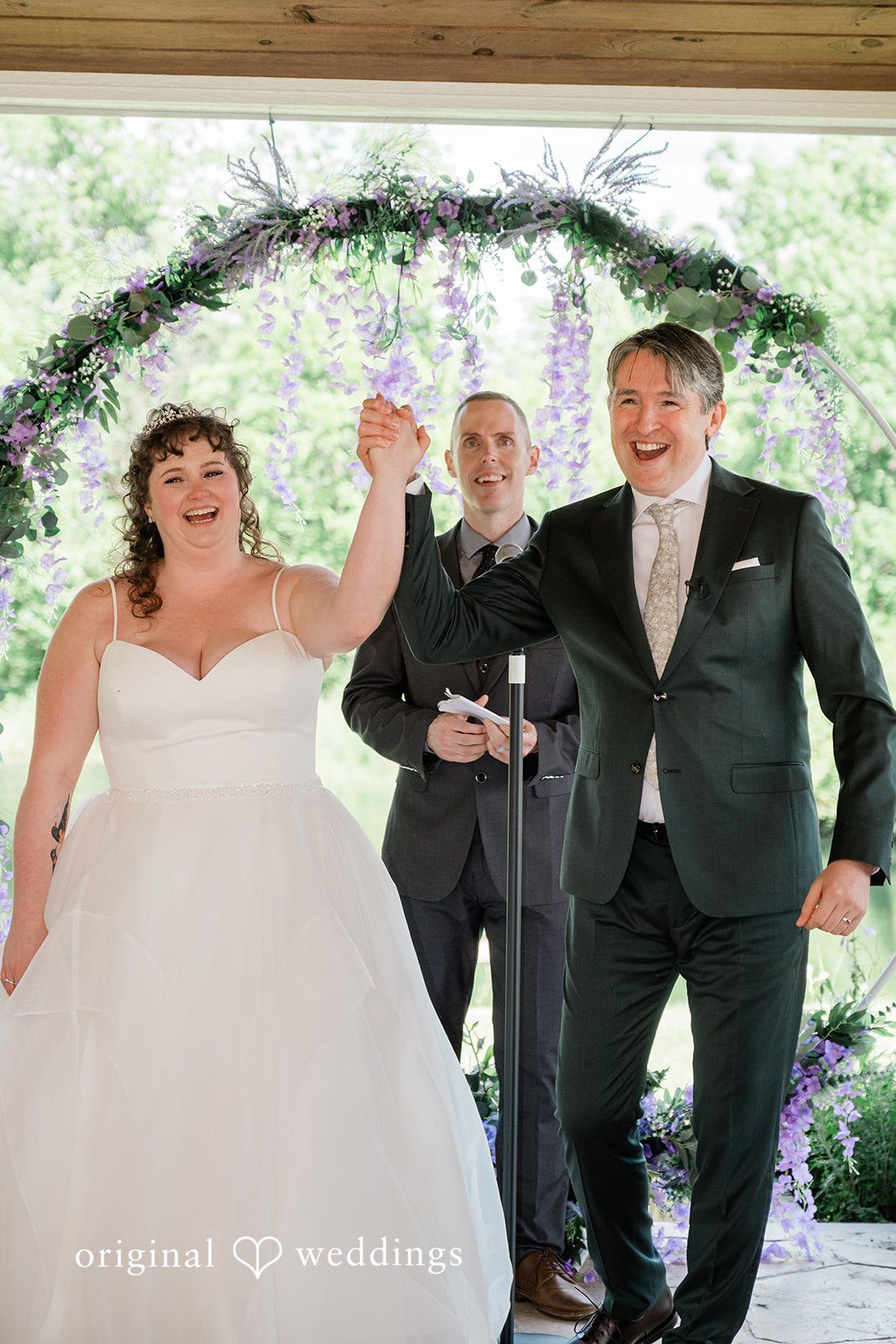 Carly + Seamus Newlyweds cheering with raised arms at the front of their ceremony.