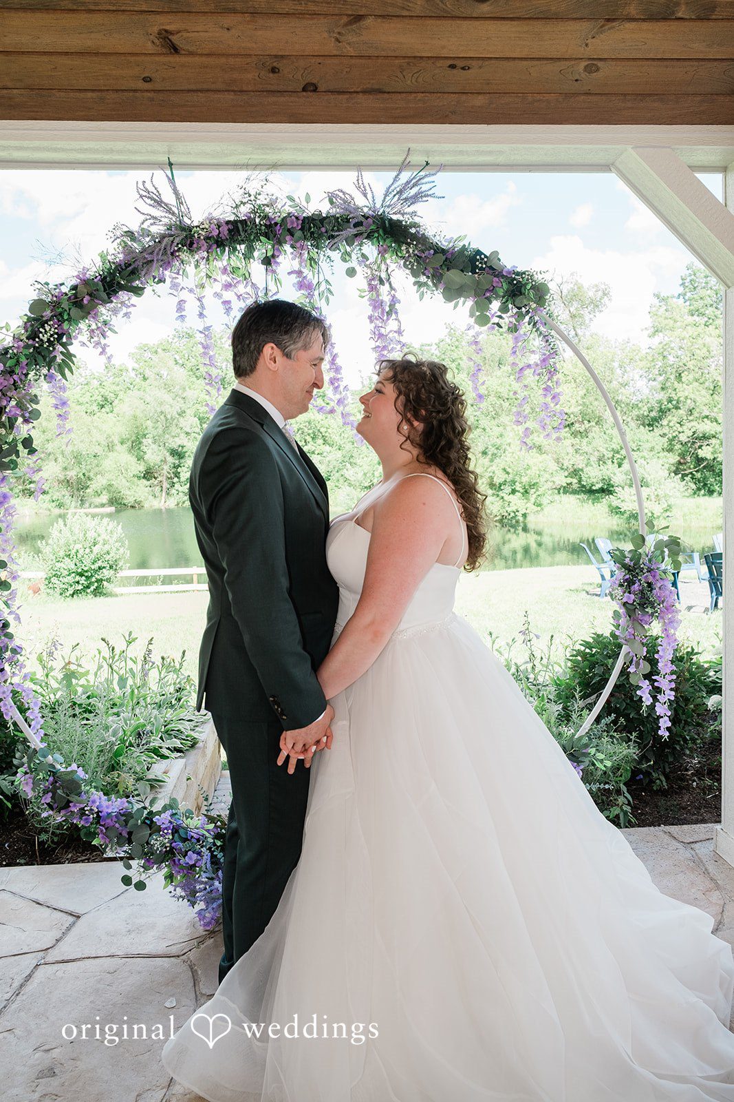 Carly + Seamus Bride and groom smiling at each other under a circular floral arch.