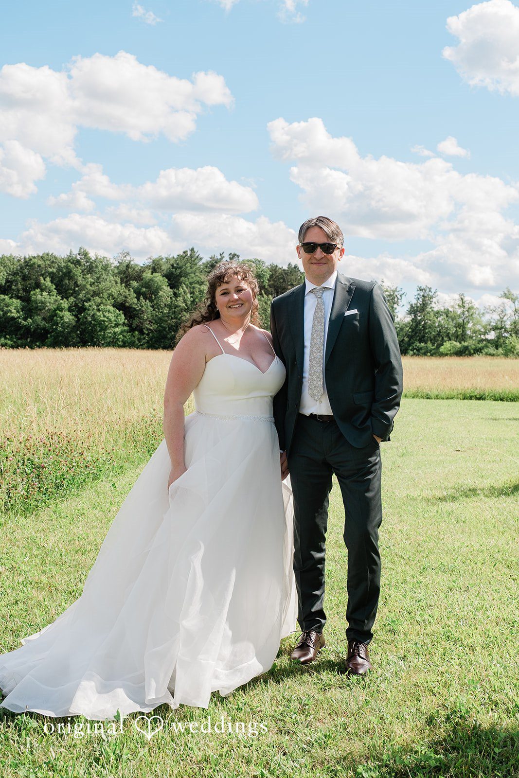 Carly + Seamus Bride and groom posing together on a grassy lawn under a blue sky.