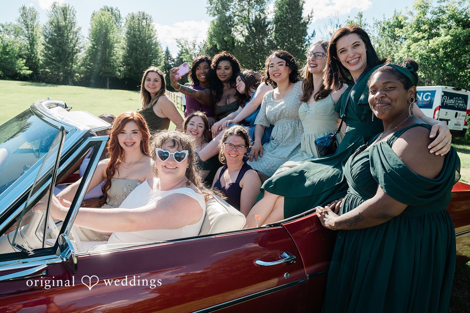Carly + Seamus Bride and bridesmaid in a white gown posing next to a vintage red convertible car.