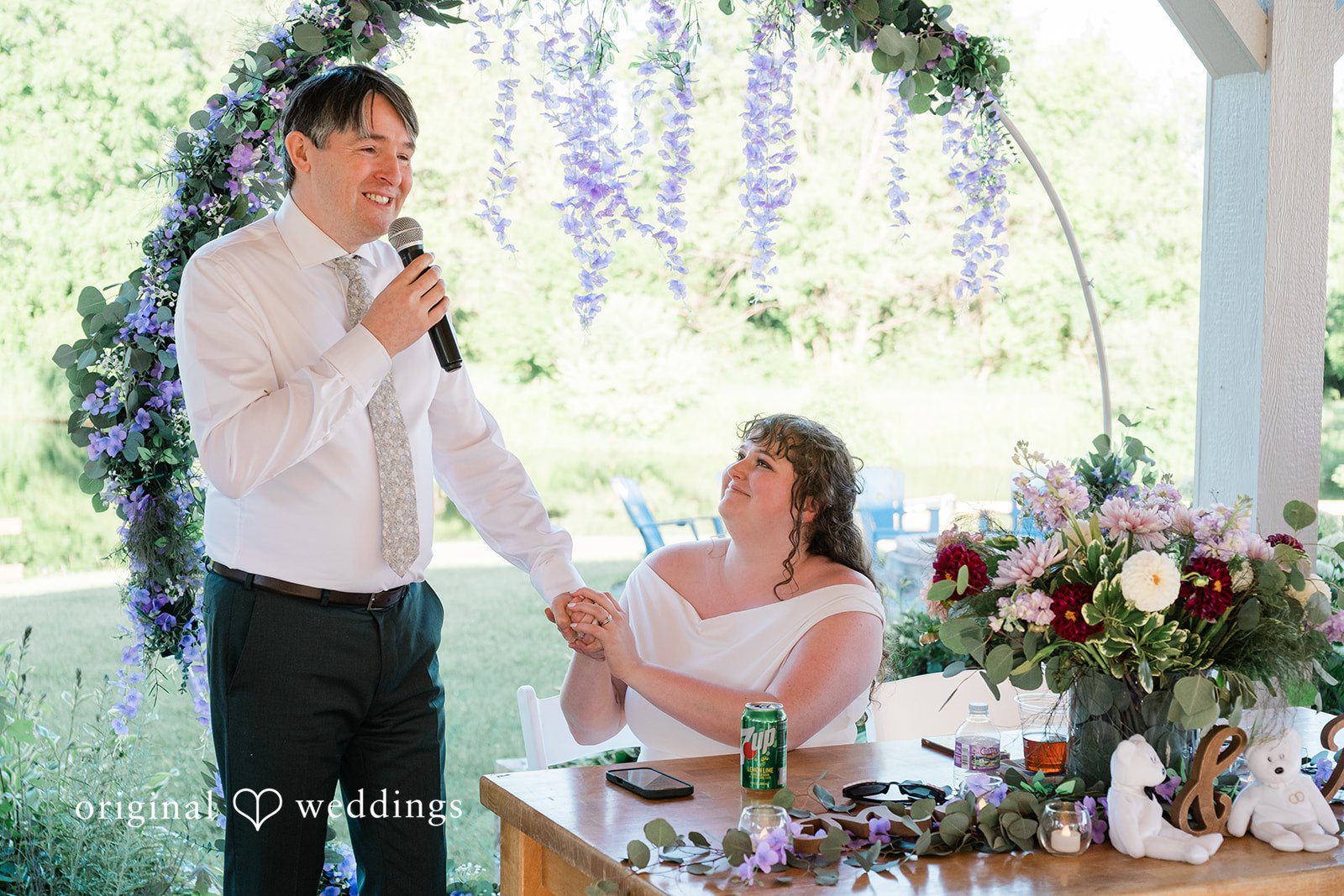 Carly + Seamus Groom speaking into a microphone while the bride sits at a decorated table.