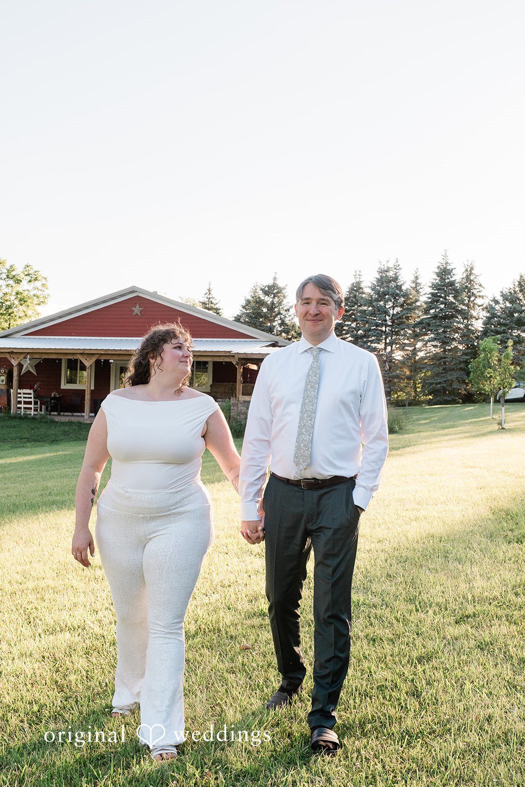 Carly + Seamus Bride wearing a white jumpsuit and groom walking side-by-side in a field.