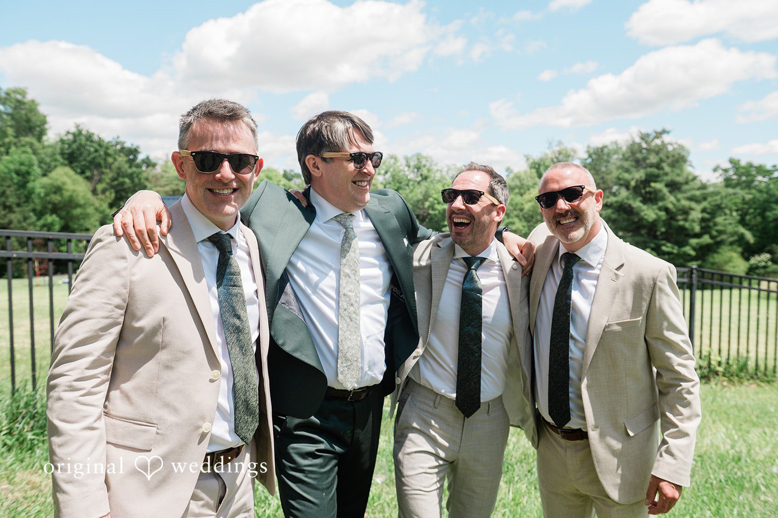 Carly + Seamus Groom and groomsmen wearing suits and sunglasses posing together on a lawn.