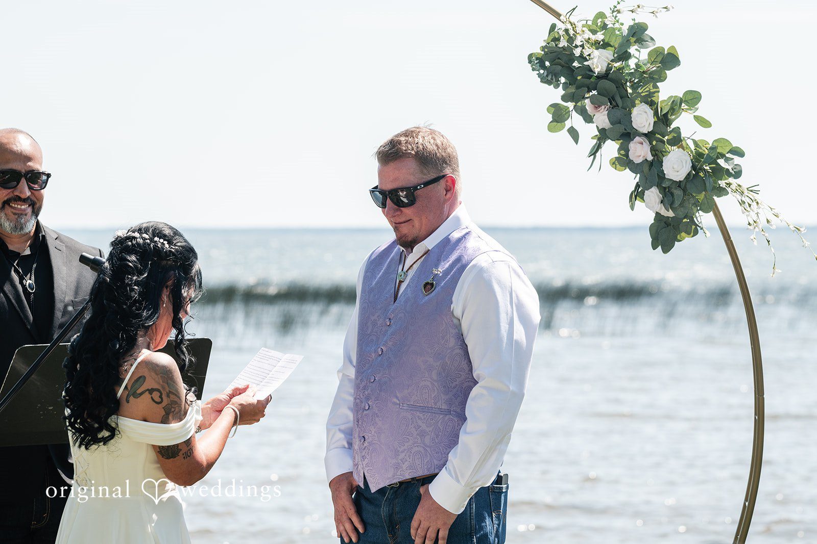 A groom in a white button-down shirt standing near the edge of a lake