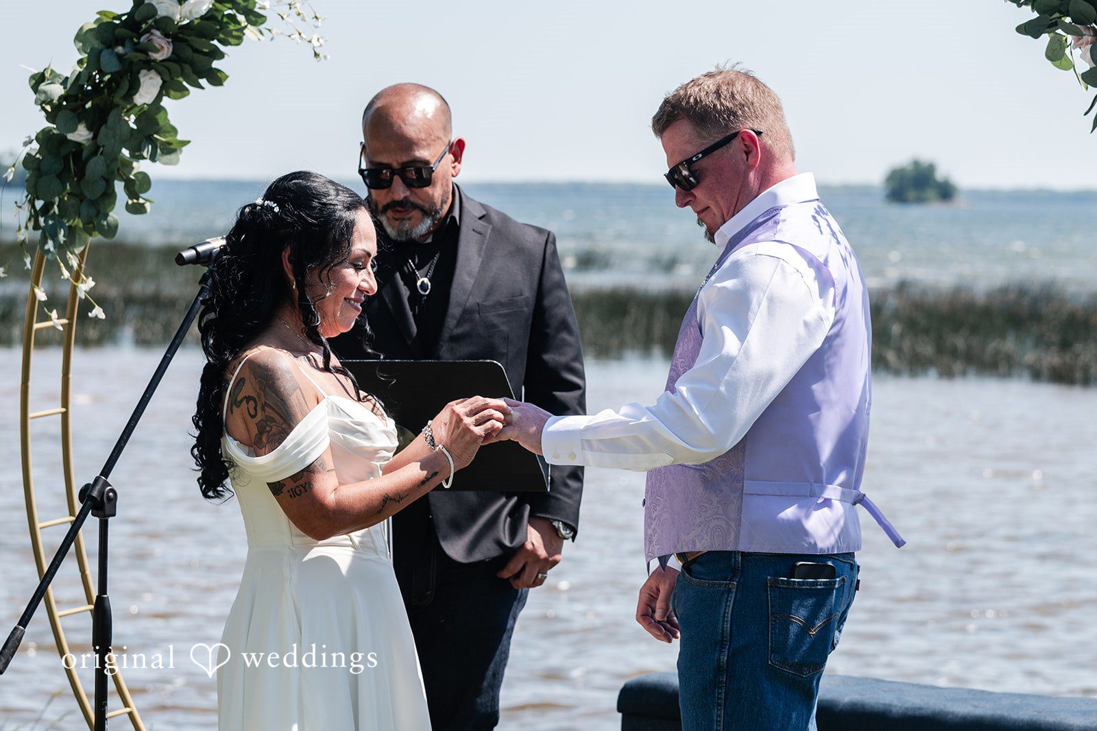 Close-up of a bride and groom exchanging rings with an officiant in the background.