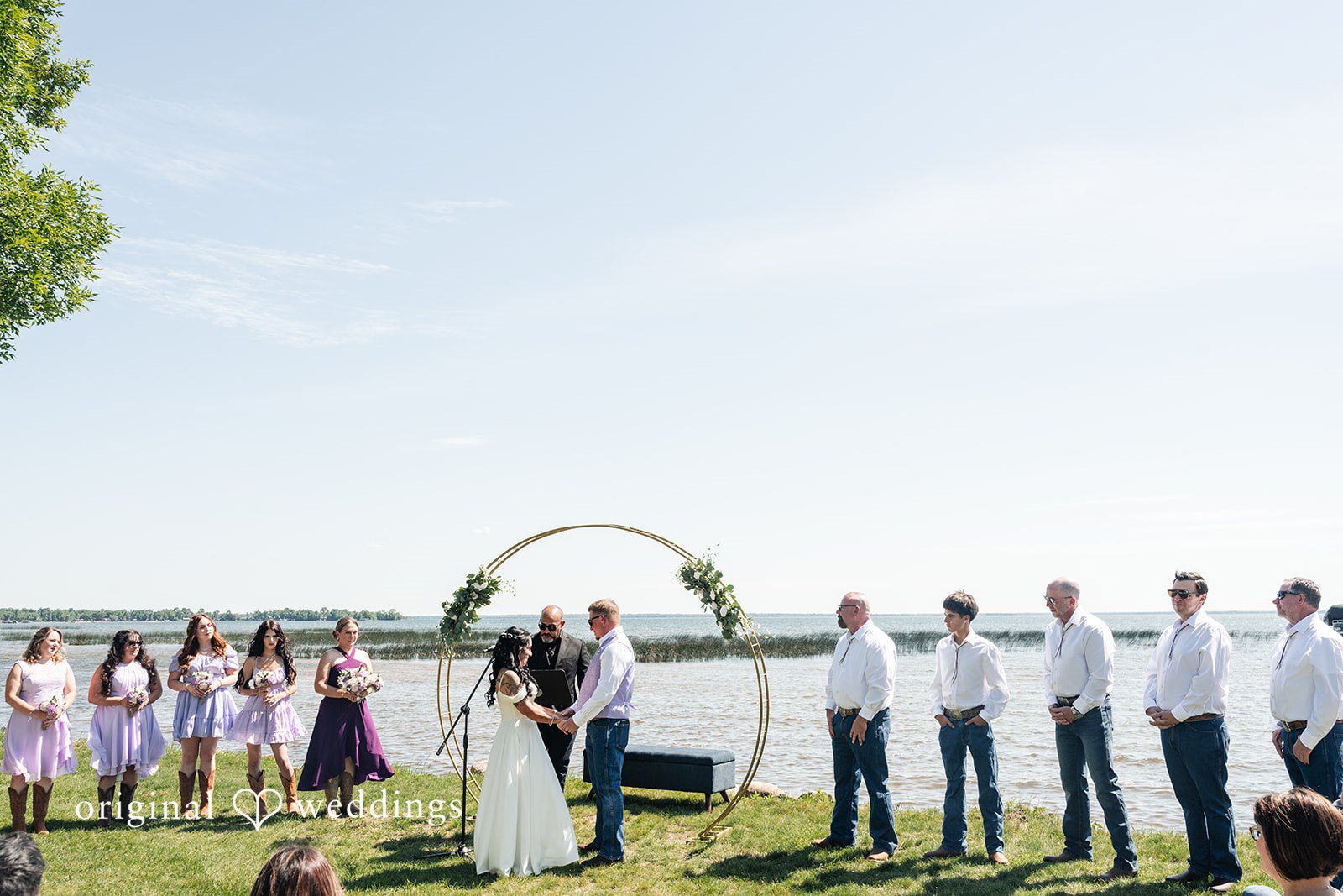Wide view of a wedding ceremony setup with guests lined up along the water.