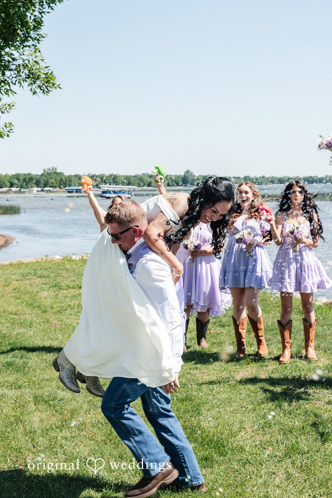 A bride running happily on a field toward her bridesmaids celebrating in the background.