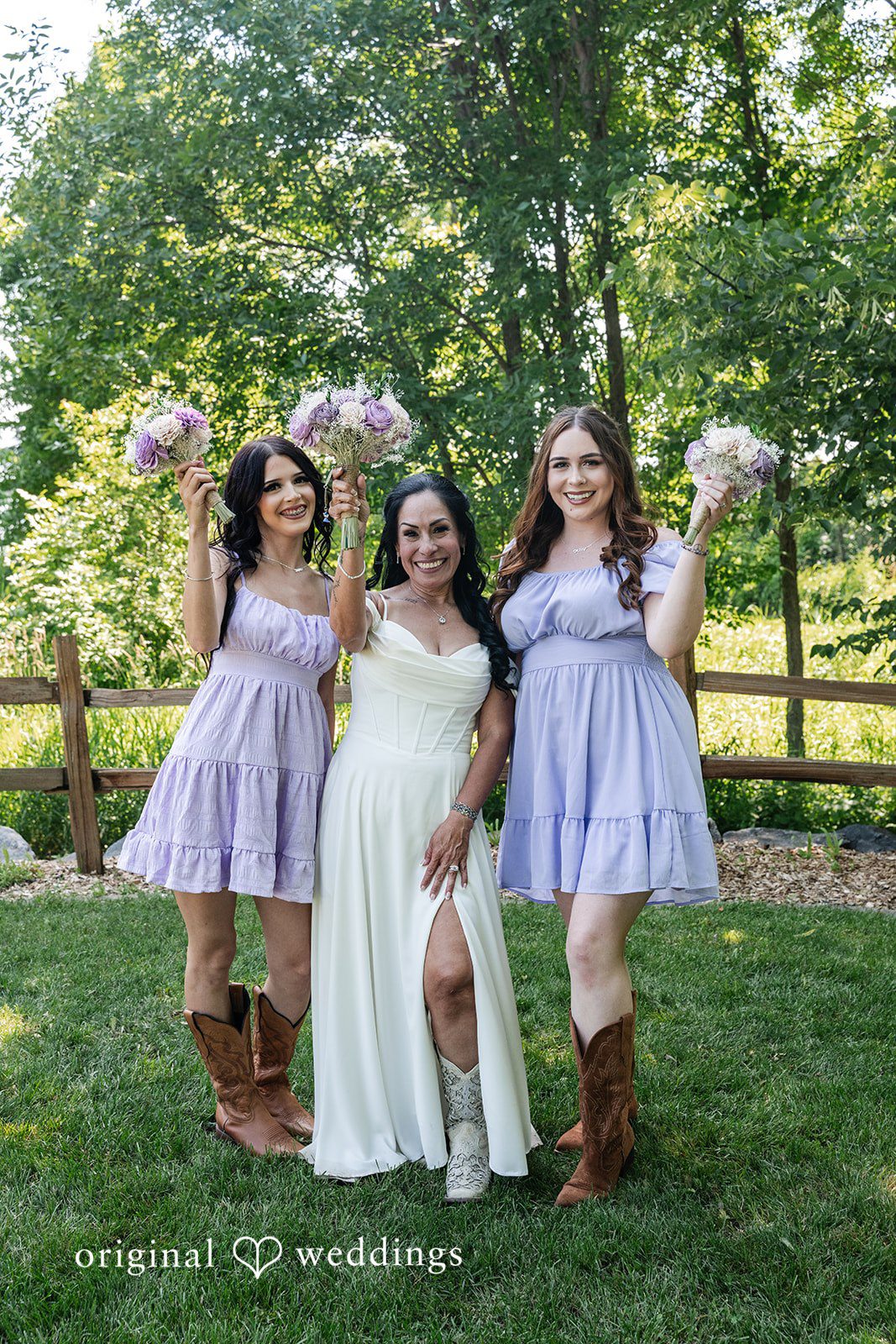 A bride and bridesmaids holding bouquets while cheering together on a lawn.