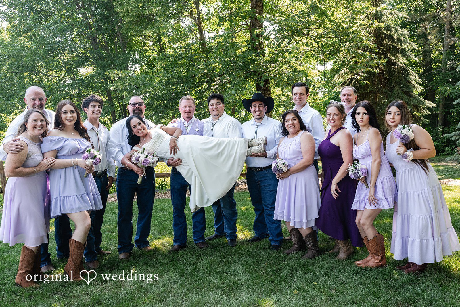 A large group of bridesmaids in purple dresses posing together on a lawn.
