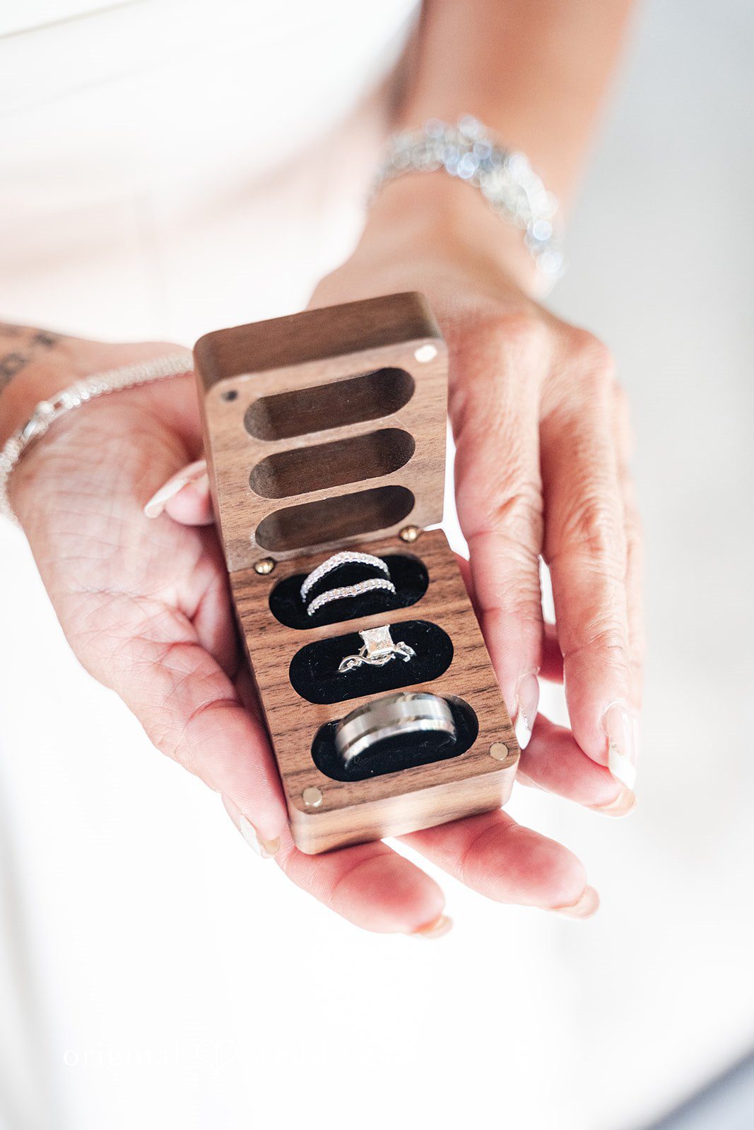 A close-up view of hands holding an open wooden box displaying rings.