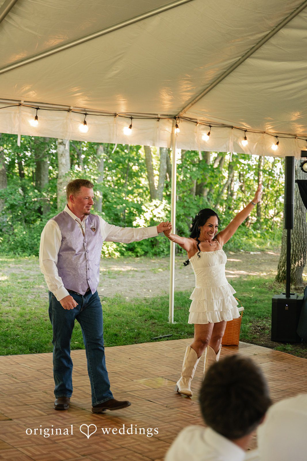 A bride dancing energetically on a dance floor under a white event canopy.