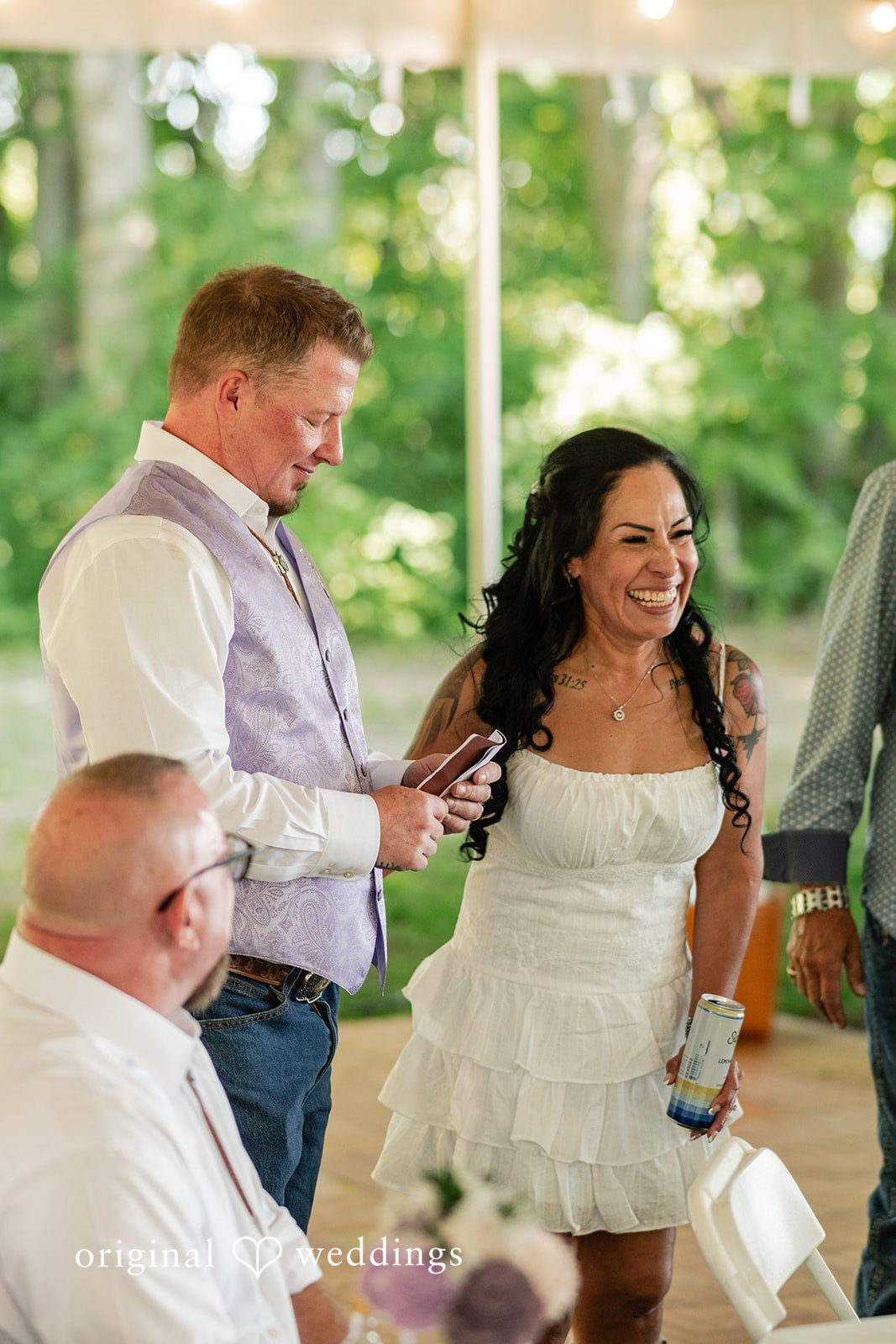 A groom in a vest looking down at a smiling bride in a white dress