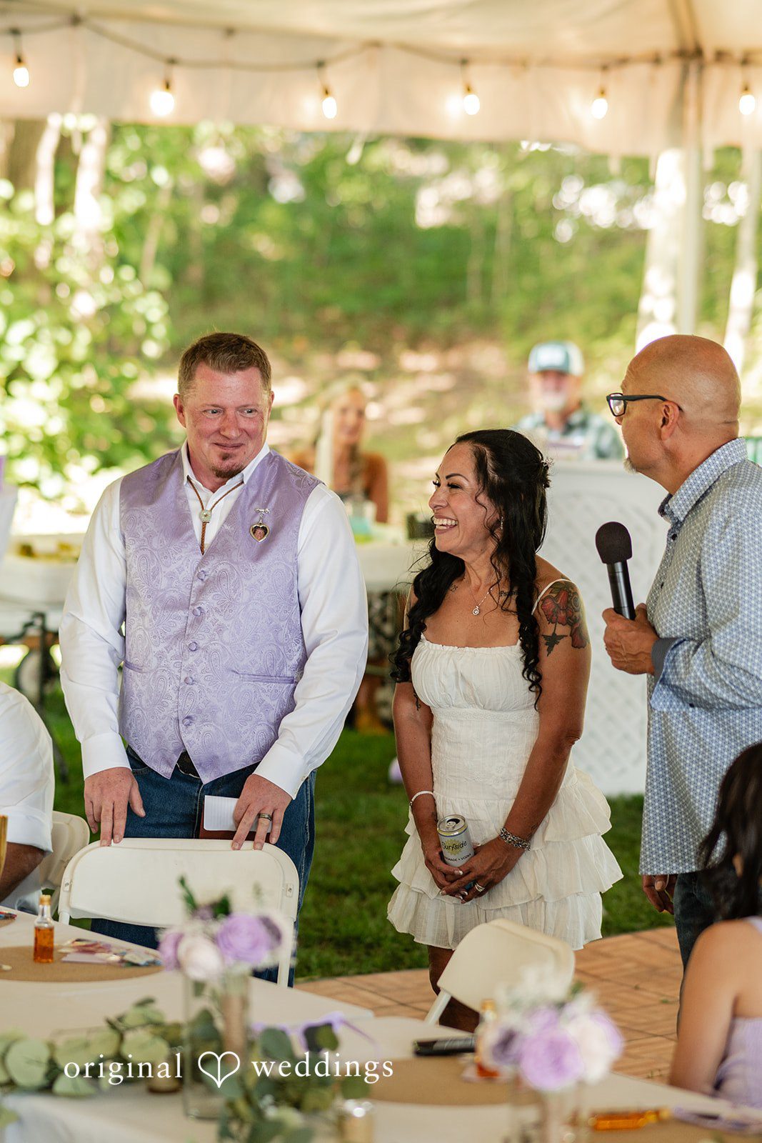 Couple listening to a speaker holding a microphone under a tent.