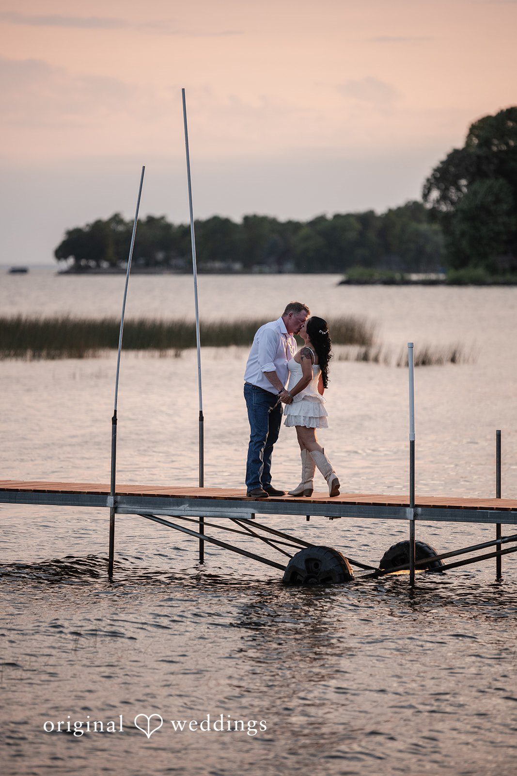 A couple sharing a kiss on a wooden dock over dark water.