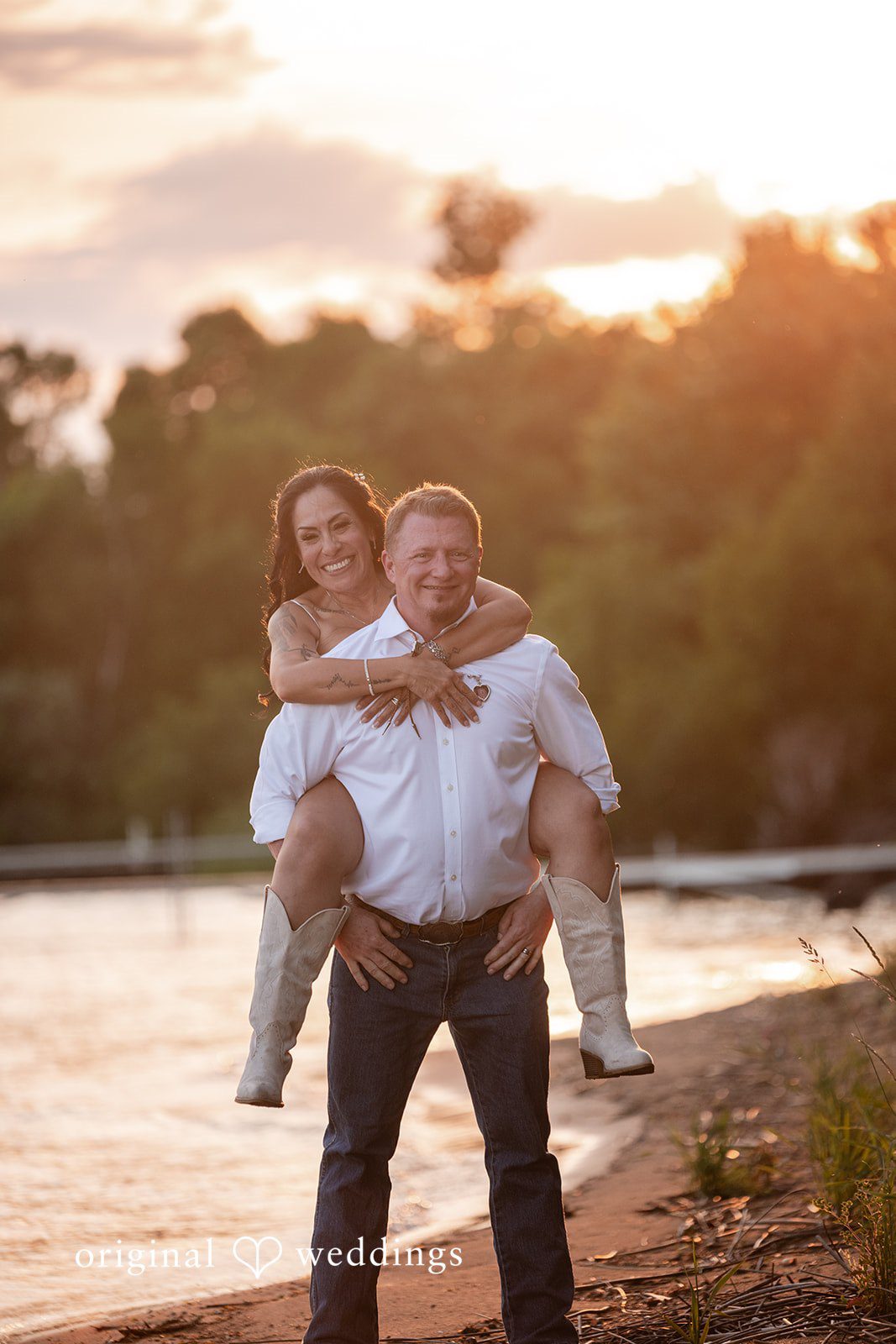 A man giving a woman a piggyback ride along a sandy shore during golden hour.