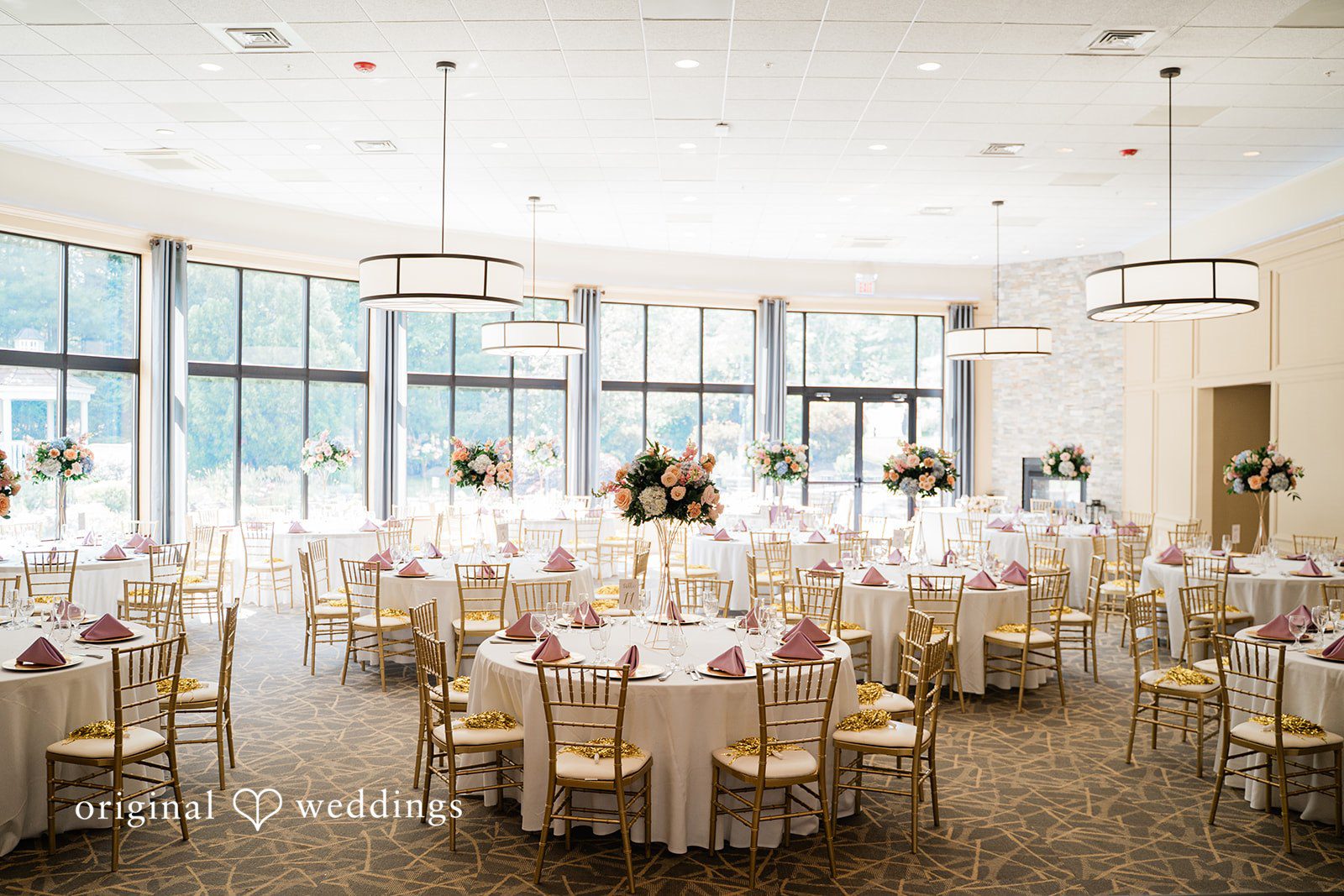 Jessica + Patrick A wide view of a wedding reception ballroom filled with decorated round tables.