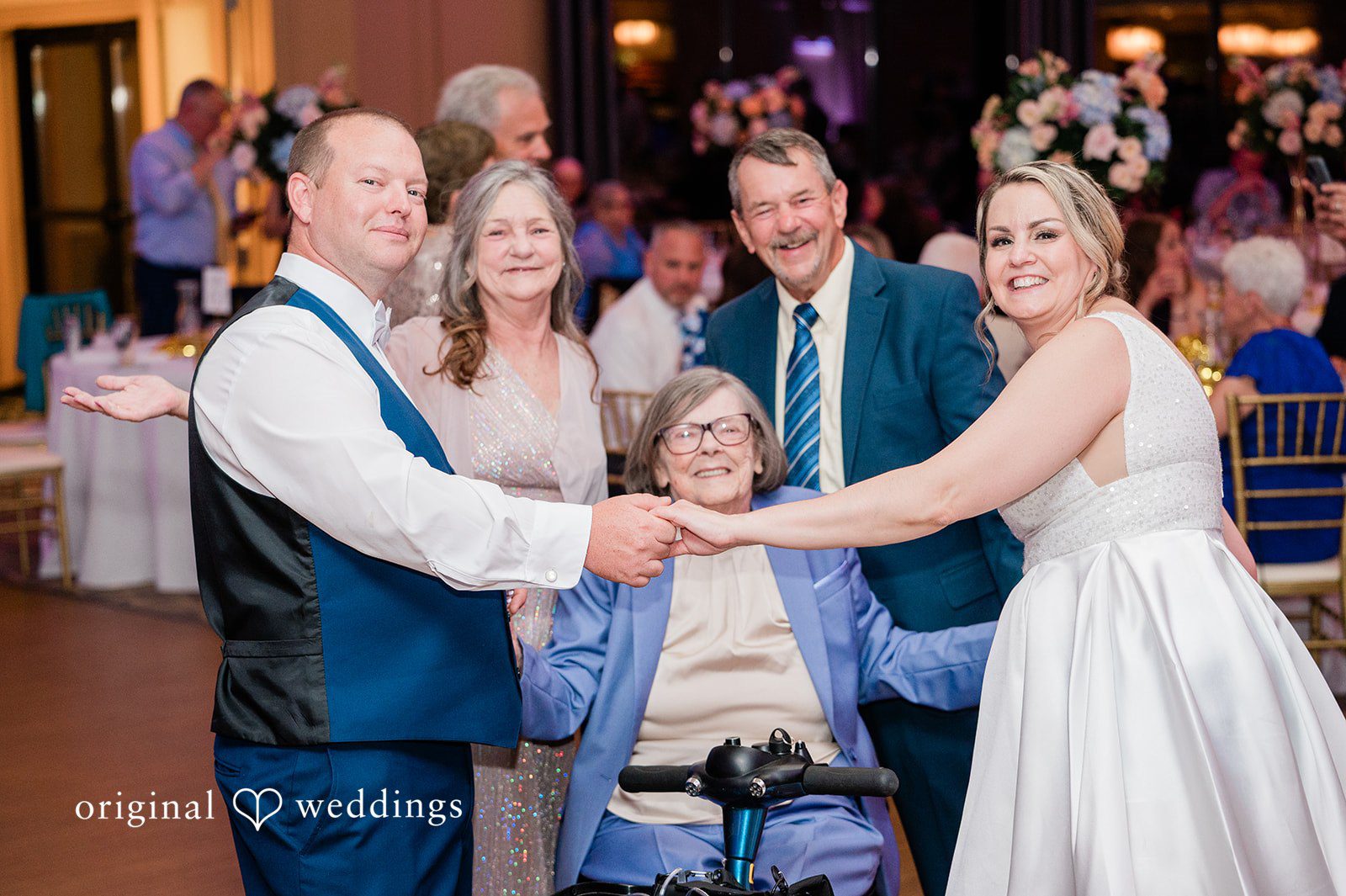 Jessica + Patrick A bride and groom hold hands with an elderly guest sitting in a wheelchair.