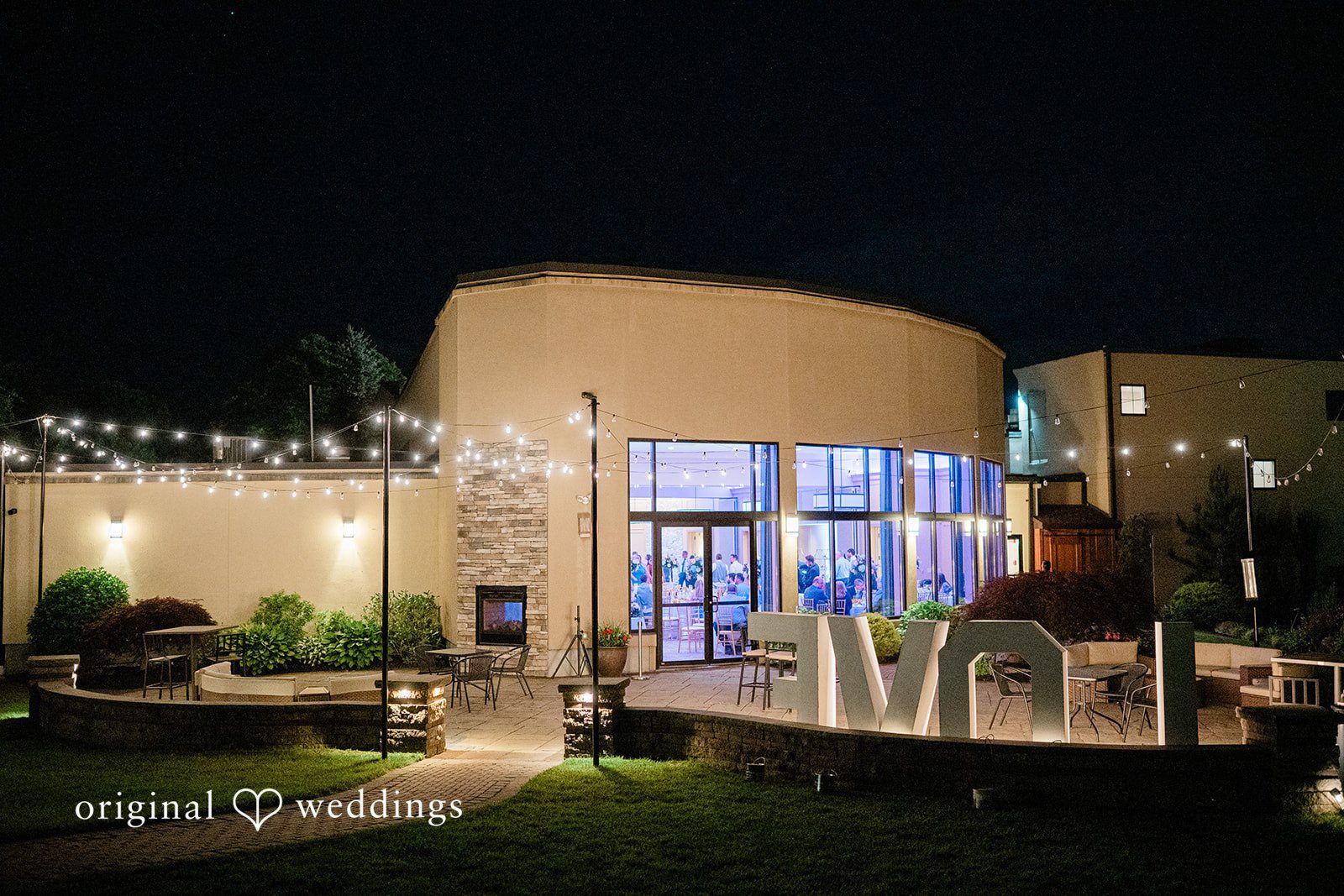 Jessica + Patrick A modern building with large glass windows lit up beautifully at night.
