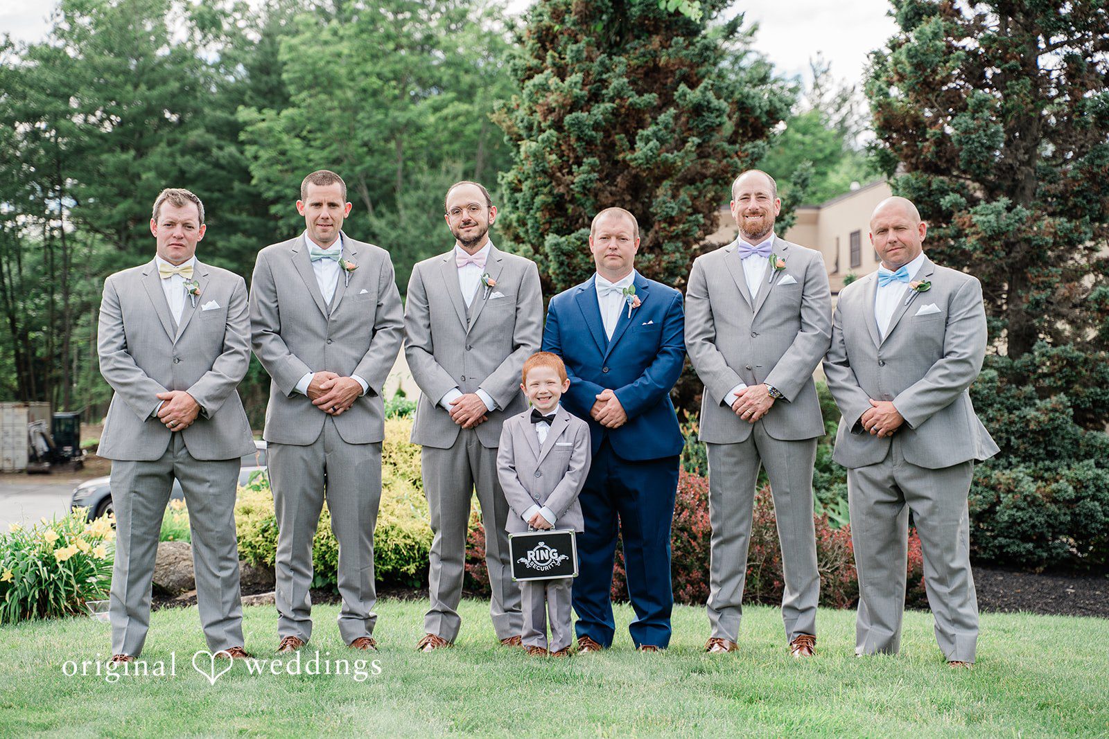 Jessica + Patrick Groom and groomsmen in matching grey suits pose together standing on a lawn.