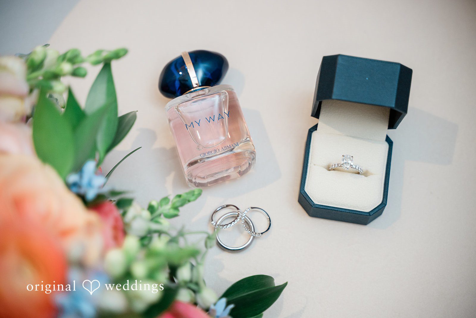 Jessica + Patrick A flat lay arrangement of bridal details including perfume, rings, and an open ring box.