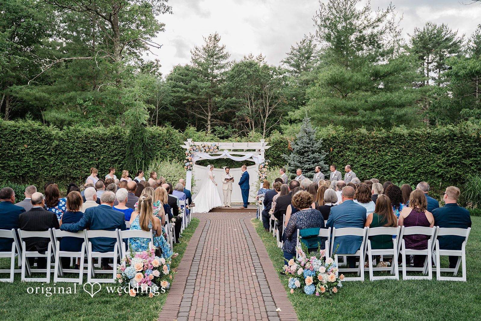 Jessica + Patrick A wide shot of a wedding ceremony taking place at an altar surrounded by guests.