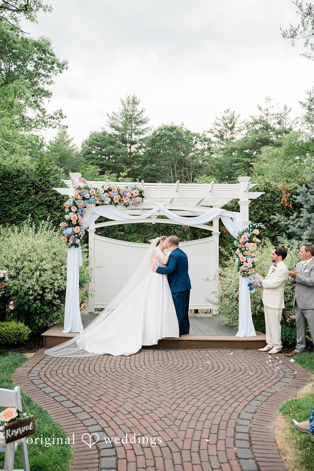 Jessica + Patrick A bride and groom share a kiss at the altar surrounded by green trees.