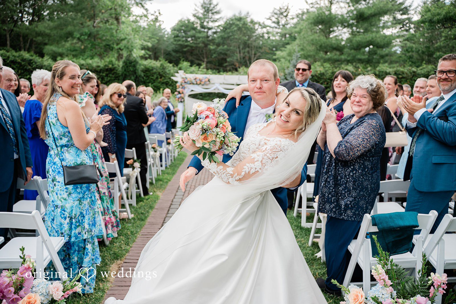 Jessica + Patrick A bride and groom smile happily while walking up the aisle as newlyweds.