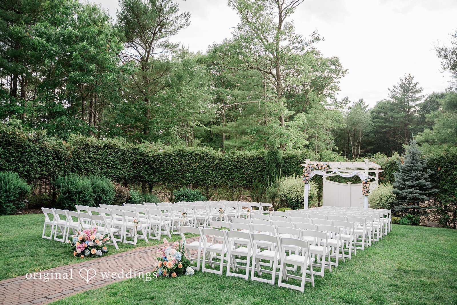 Jessica + Patrick Rows of white folding chairs set up on a lawn for a wedding ceremony.