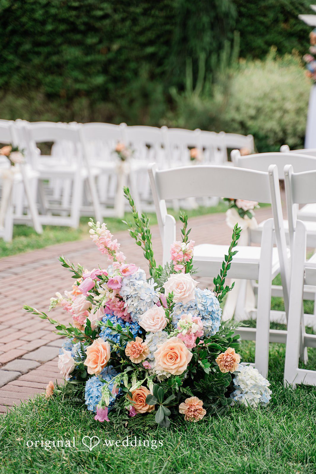 Jessica + Patrick A vibrant floral arrangement placed on the grass next to white ceremony chairs.