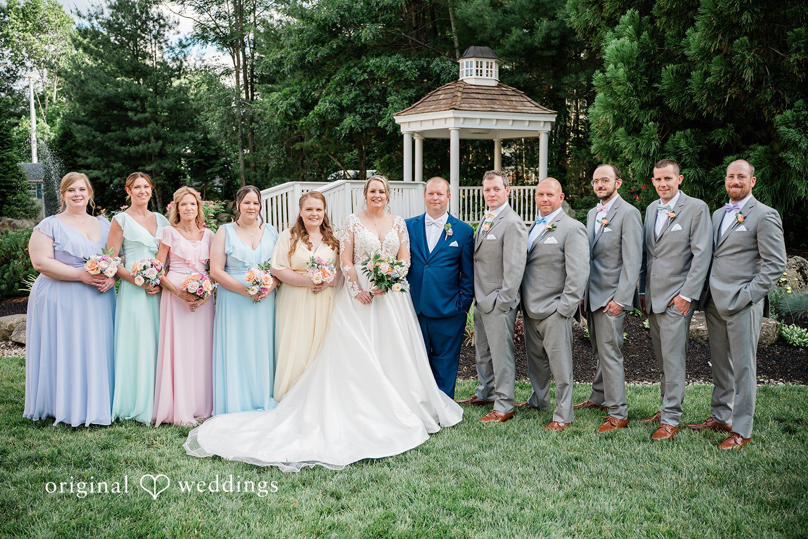 Jessica + Patrick A large wedding party poses together on a lawn in front of a gazebo.