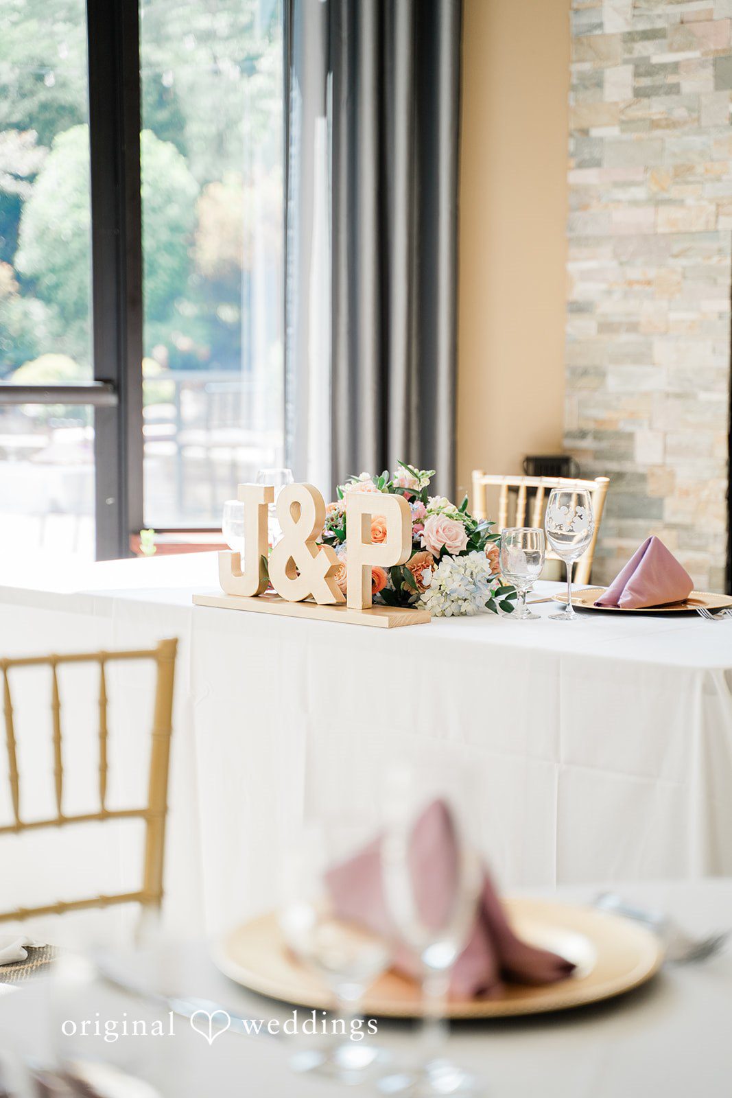 Jessica + Patrick A close-up of a reception table setting with a pink cloth napkin on a gold charger plate.