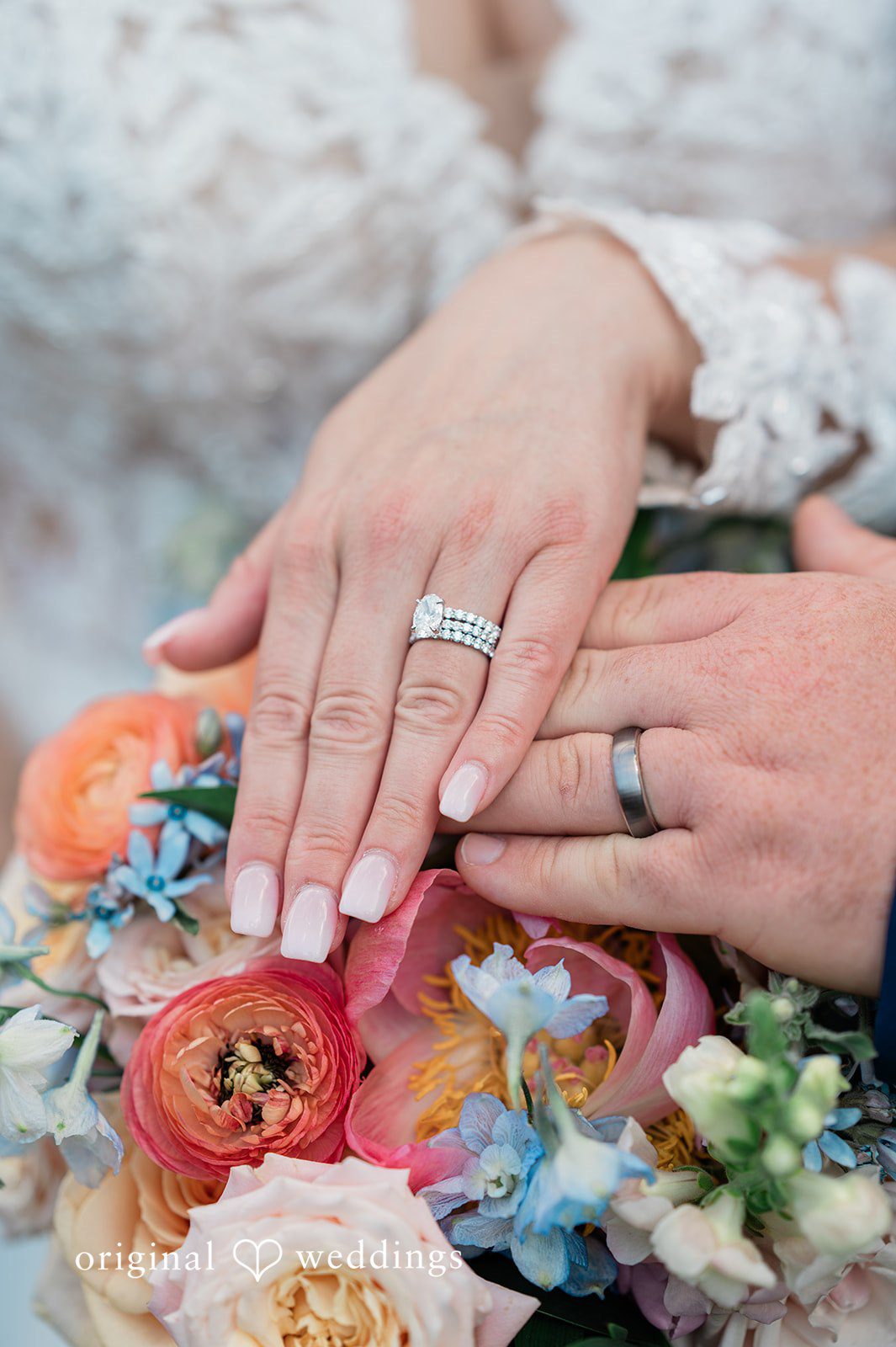 Jessica + Patrick A close-up view of two hands showing off wedding rings over a vibrant floral bouquet.