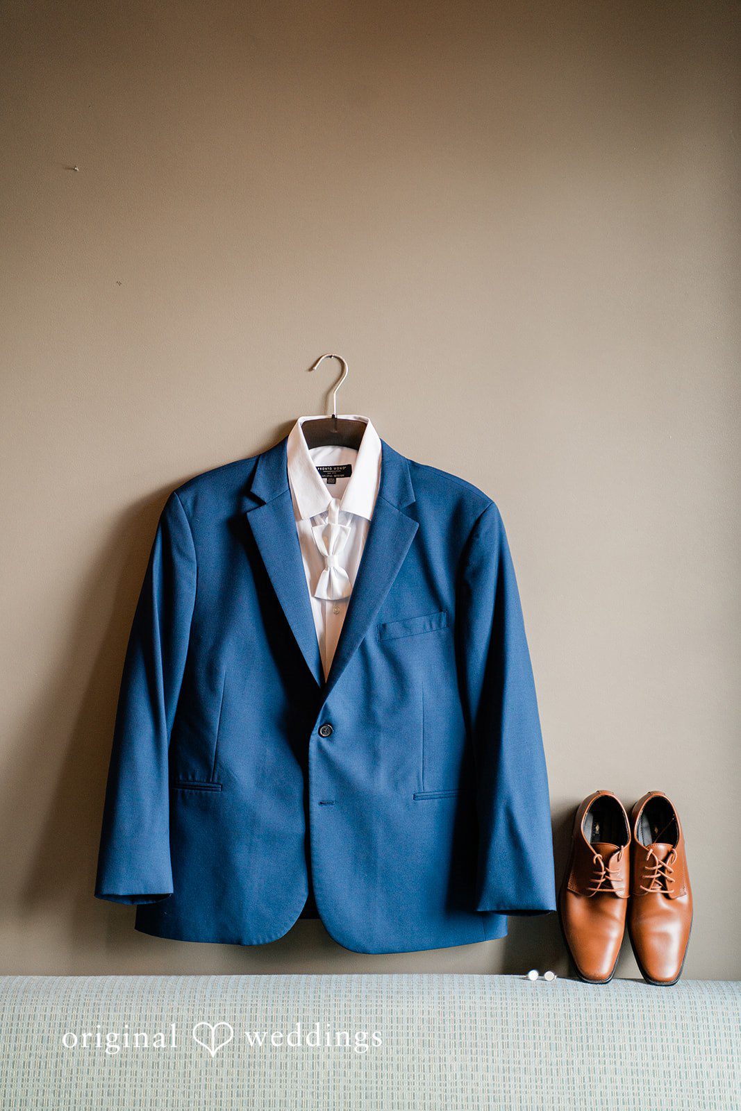 Jessica + Patrick A blue suit jacket hanging on a wall next to a pair of brown leather shoes.