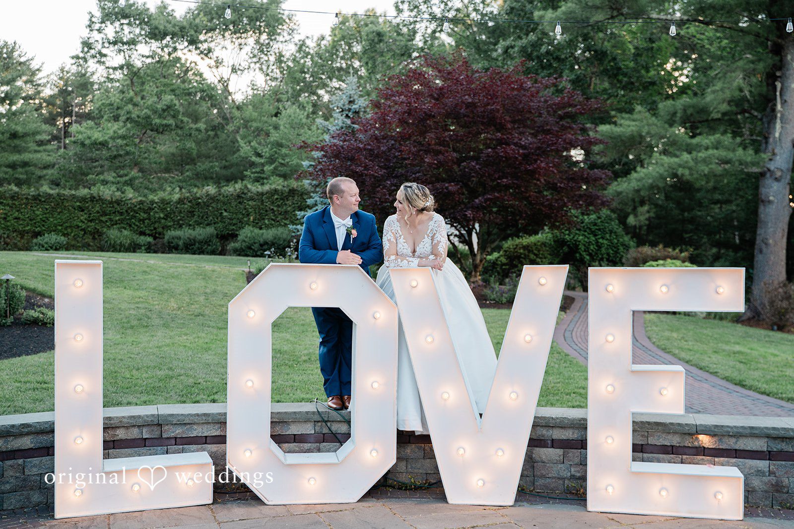 Jessica + Patrick A bride and groom pose behind large, glowing letters that spell out the word love.