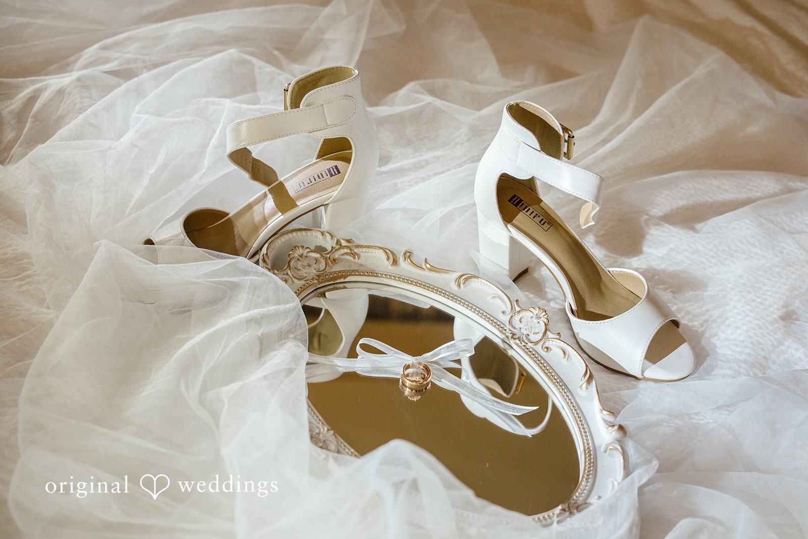 Emily + Maxwell A pair of white bridal heels resting on top of a delicate lace wedding veil.