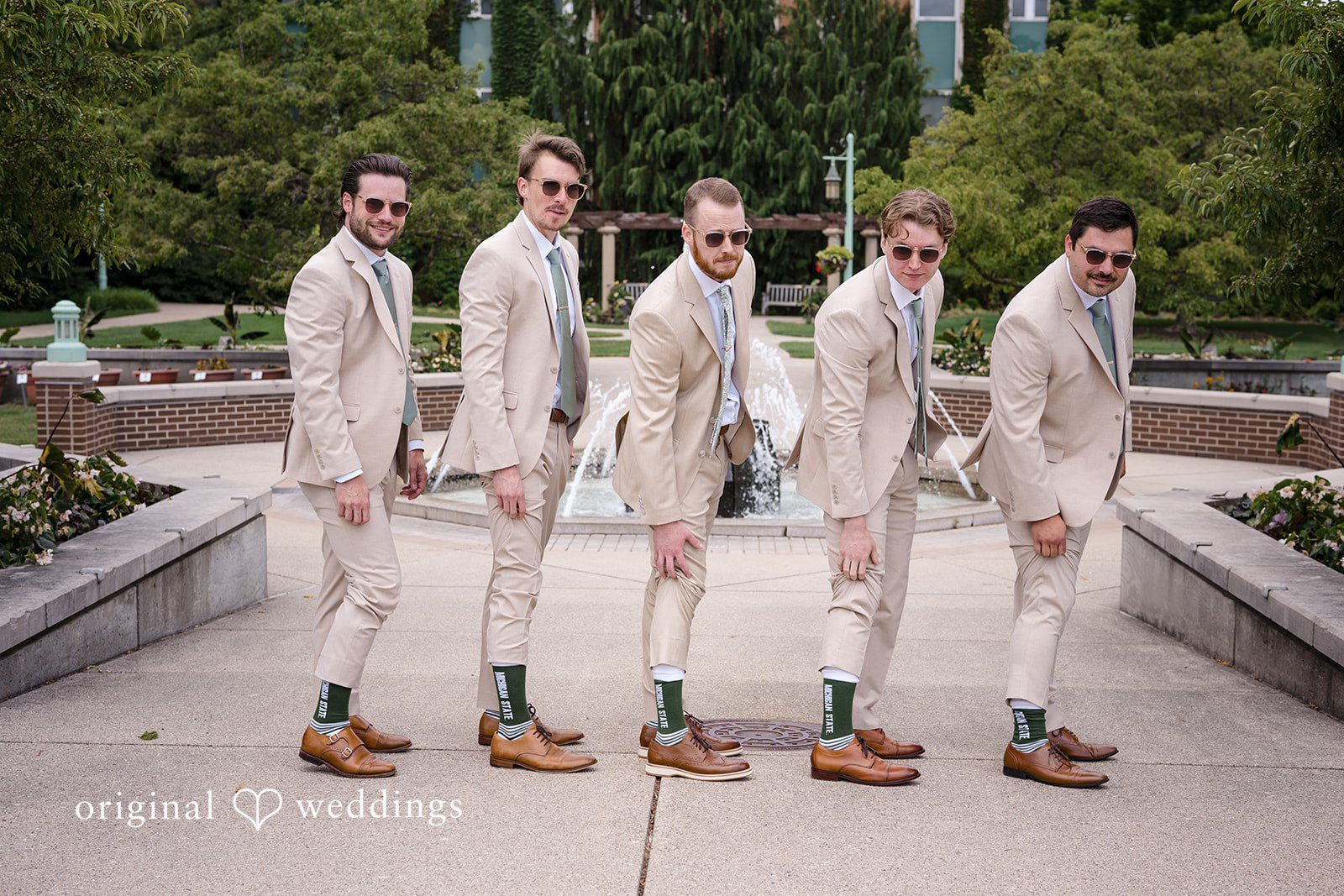 Emily + Maxwell Groom and groomsmen in light-colored suits standing in a row next to a brick path.