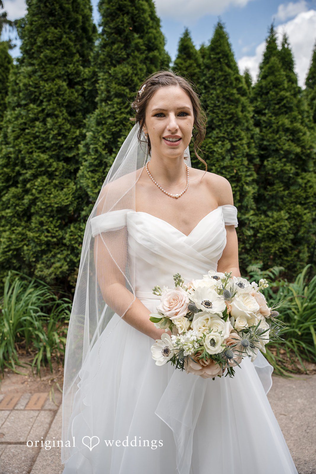Emily + Maxwell A bride posing in her white gown while holding a large bouquet of white flowers.