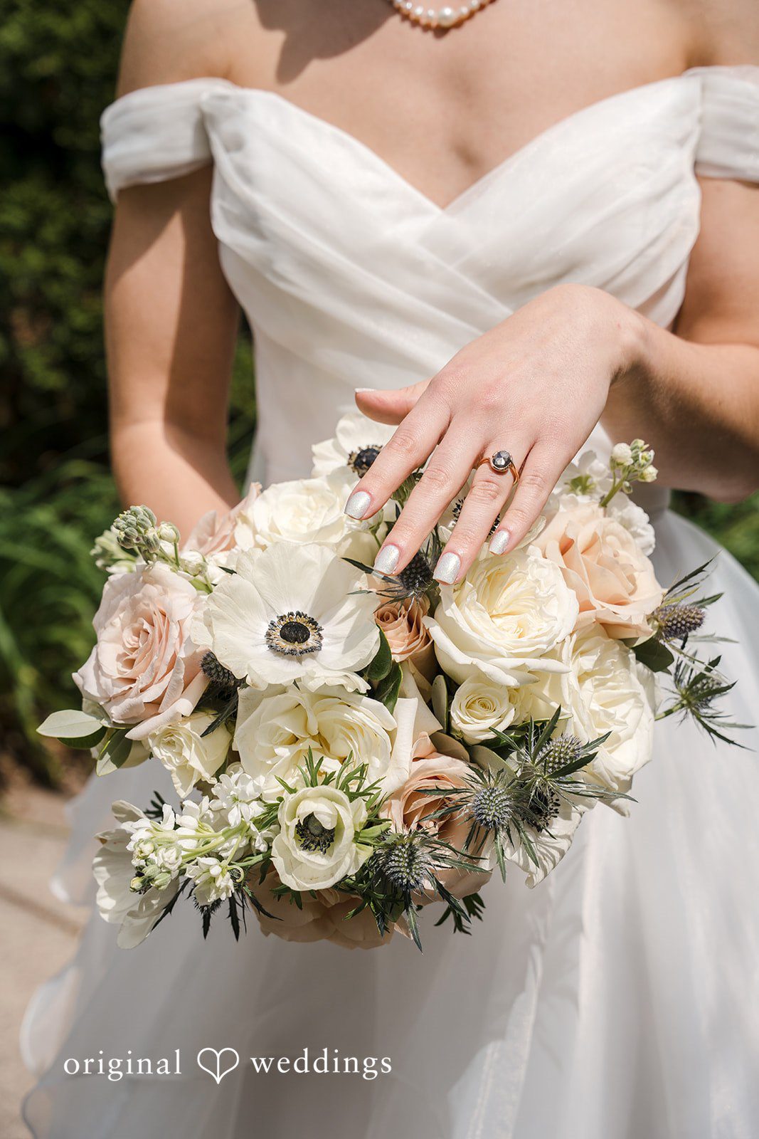 Emily + Maxwell A close-up of a bride holding a bouquet filled with white roses and green foliage.