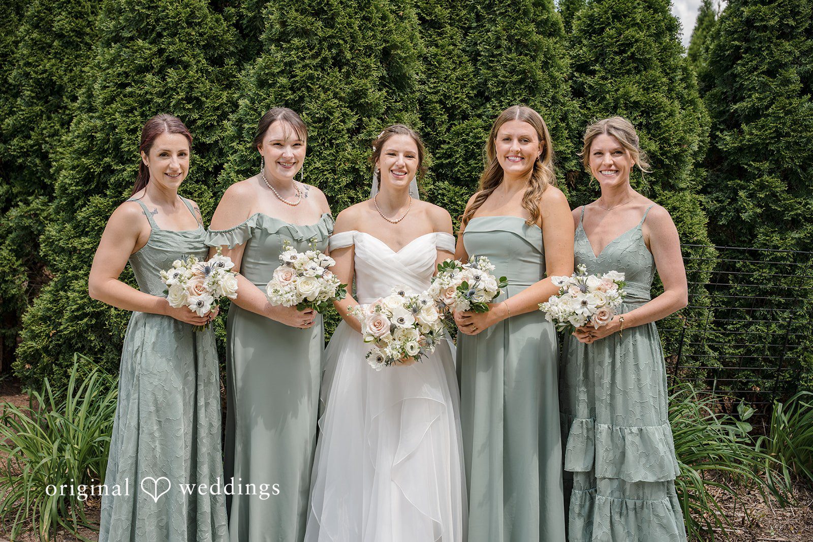 Emily + Maxwell A bride and four bridesmaids in sage green dresses posing together in a line.